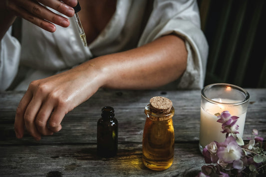 A person applying oil from a glass dropper onto their arm at a table
